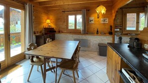 Eine Holzhütte mit Esstisch, Stühlen, einer Küchenzeile und großen Fenstern.