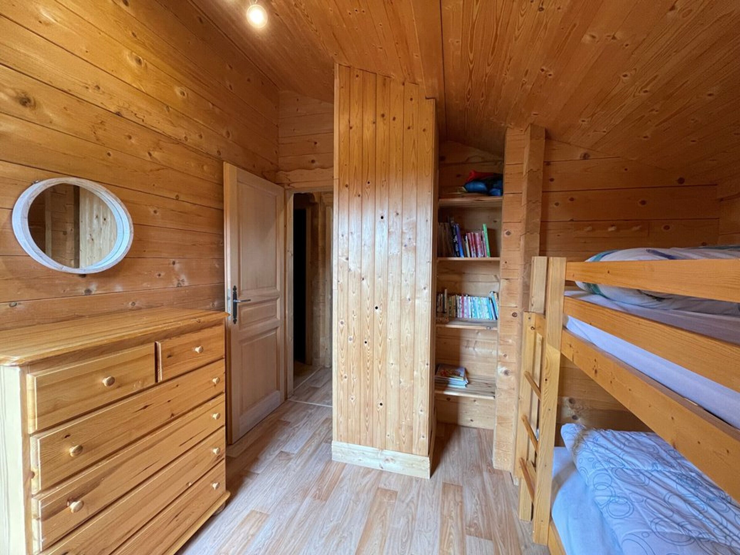 A wooden interior with a bunk bed, a circular mirror, and a wardrobe.