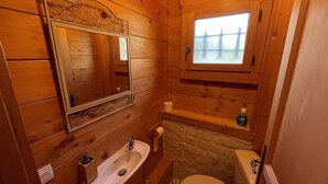 Ein kleines Badezimmer aus Holz mit Waschbecken, Toilette und einem Fenster über der Toilette.