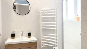 Ein Badezimmer mit einem weißen Waschbecken, zwei schwarzen Seifenspendern, einem runden Spiegel und einem weißen Handtuchwärmer.
