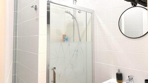 Un baño moderno con cabina de ducha de vidrio, un espejo redondo y un lavabo blanco.