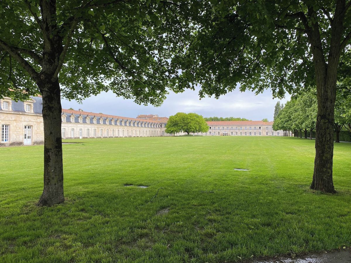 Une vaste étendue d’herbe, un espace dégagé, avec un bâtiment historique en arrière-plan.