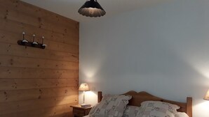 Une chambre avec un mur en bois, un lit recouvert d’une literie à motifs floraux, deux lampes de chevet et un luminaire au plafond.