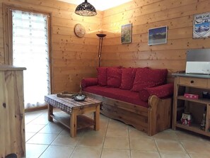 Um quarto aconchegante com paredes de madeira, um sofá vermelho, uma mesa de madeira com toalha xadrez, um abajur e um relógio.
