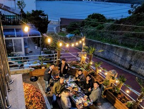 A rooftop dining area with string lights, outdoor seating, and a view of the surrounding landscape. - Relax and Enjoy the Beauty of Bird Song and Crashing Waves (Geoje-si)