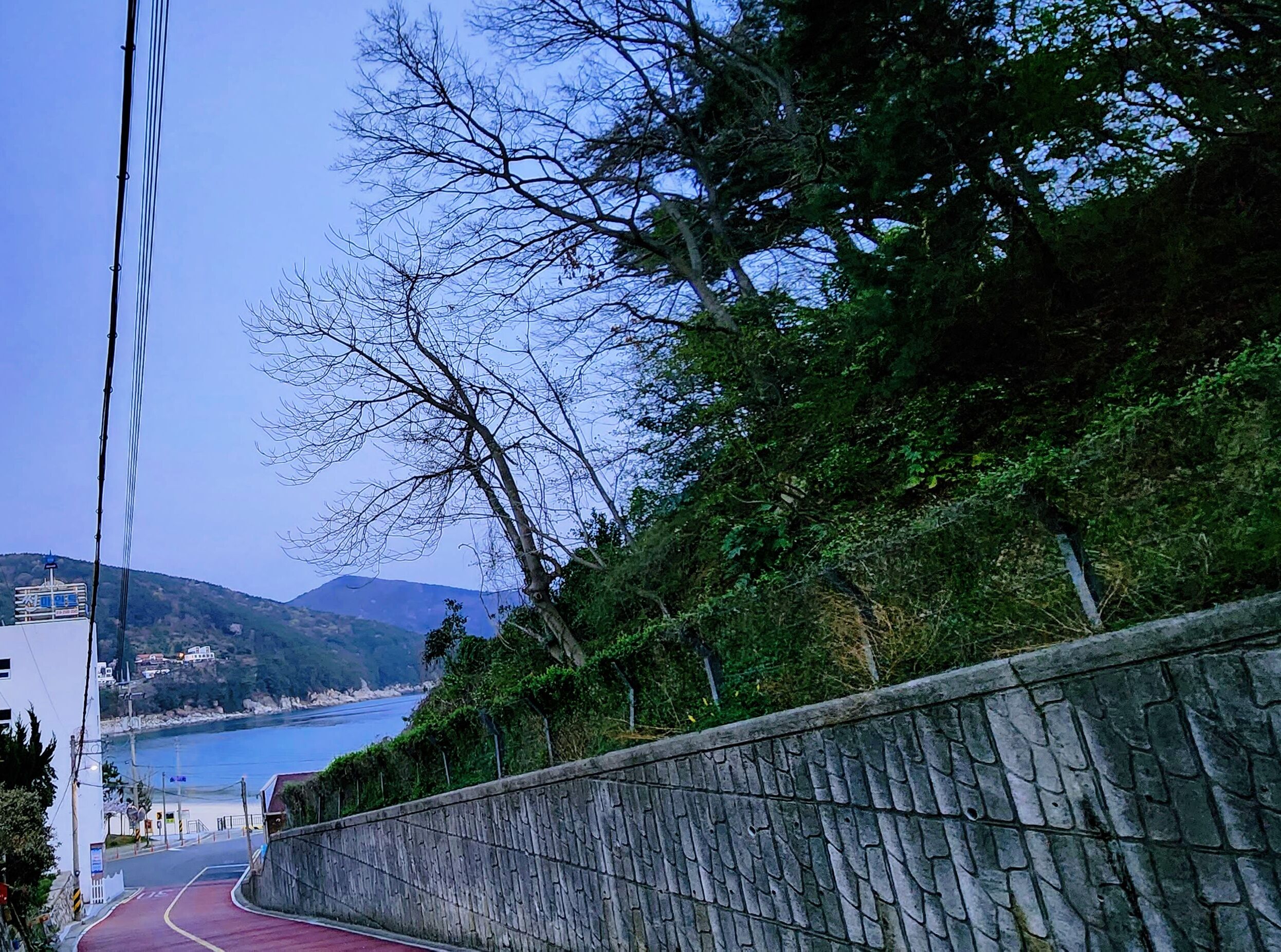 A coastal road with a stone wall on one side and a view of the sea and hills in the distance.
