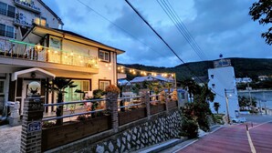 A two-story building with a balcony, a sign indicating a restaurant, and a view of the sea.