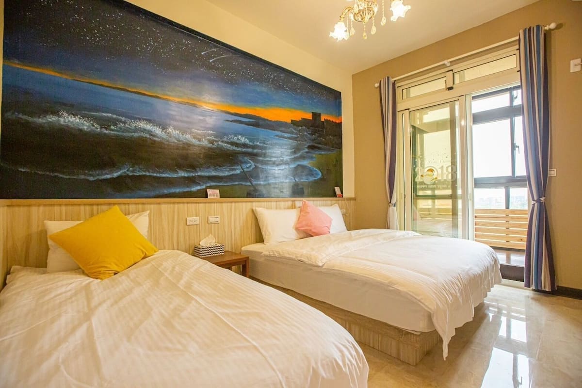A hotel room with two beds, a night sky mural, a chandelier, and a balcony with curtains.