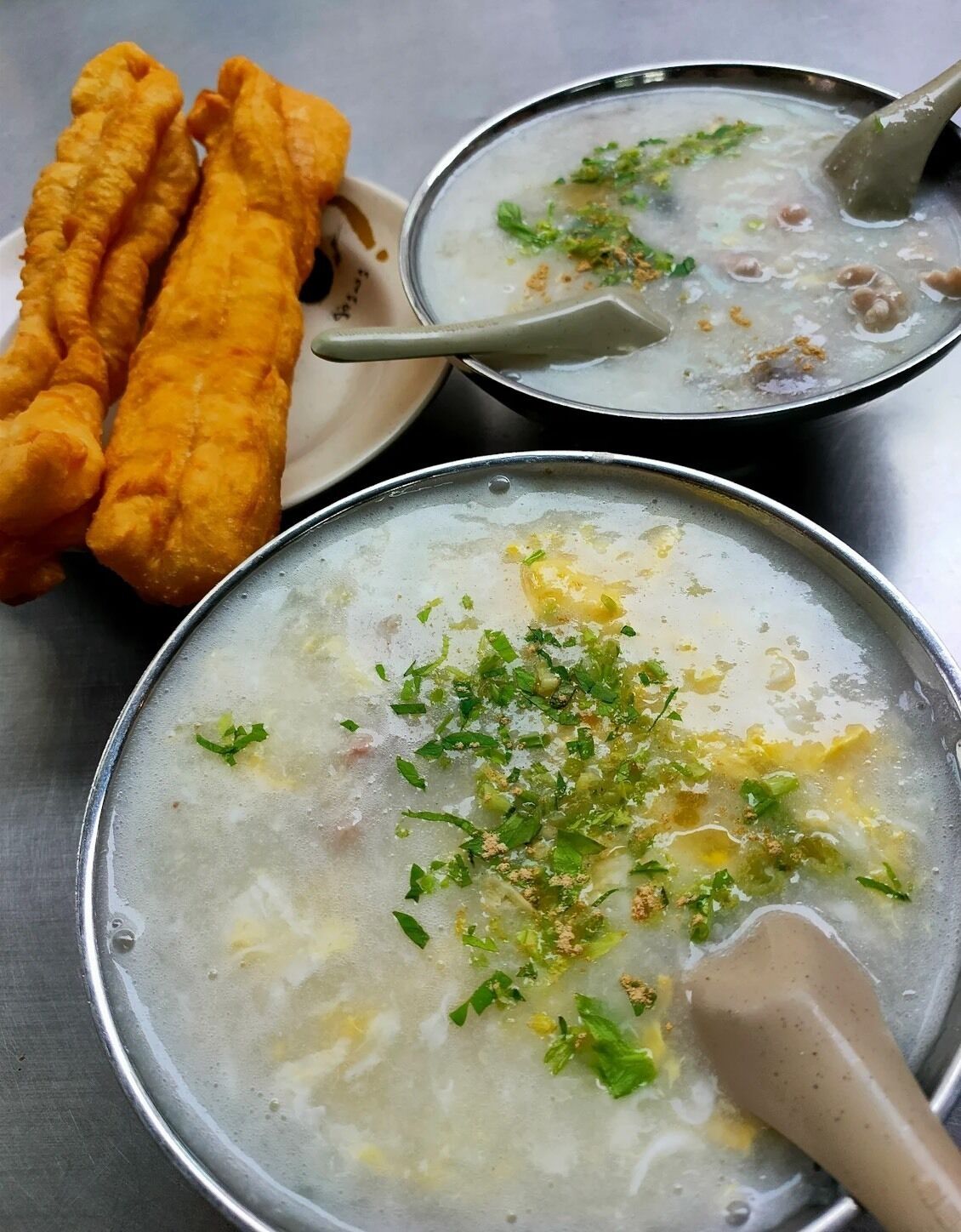 Dos tazones de sopa con una espumadera, adornados con hierbas, y un plato de frituras a un lado.