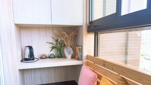 Habitación compacta con un banco de madera, una pequeña estantería con objetos decorativos y una ventana con vistas al exterior.