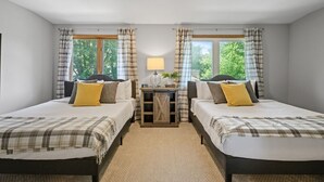 A double room with two beds, a small table with a lamp, and a view of greenery outside.