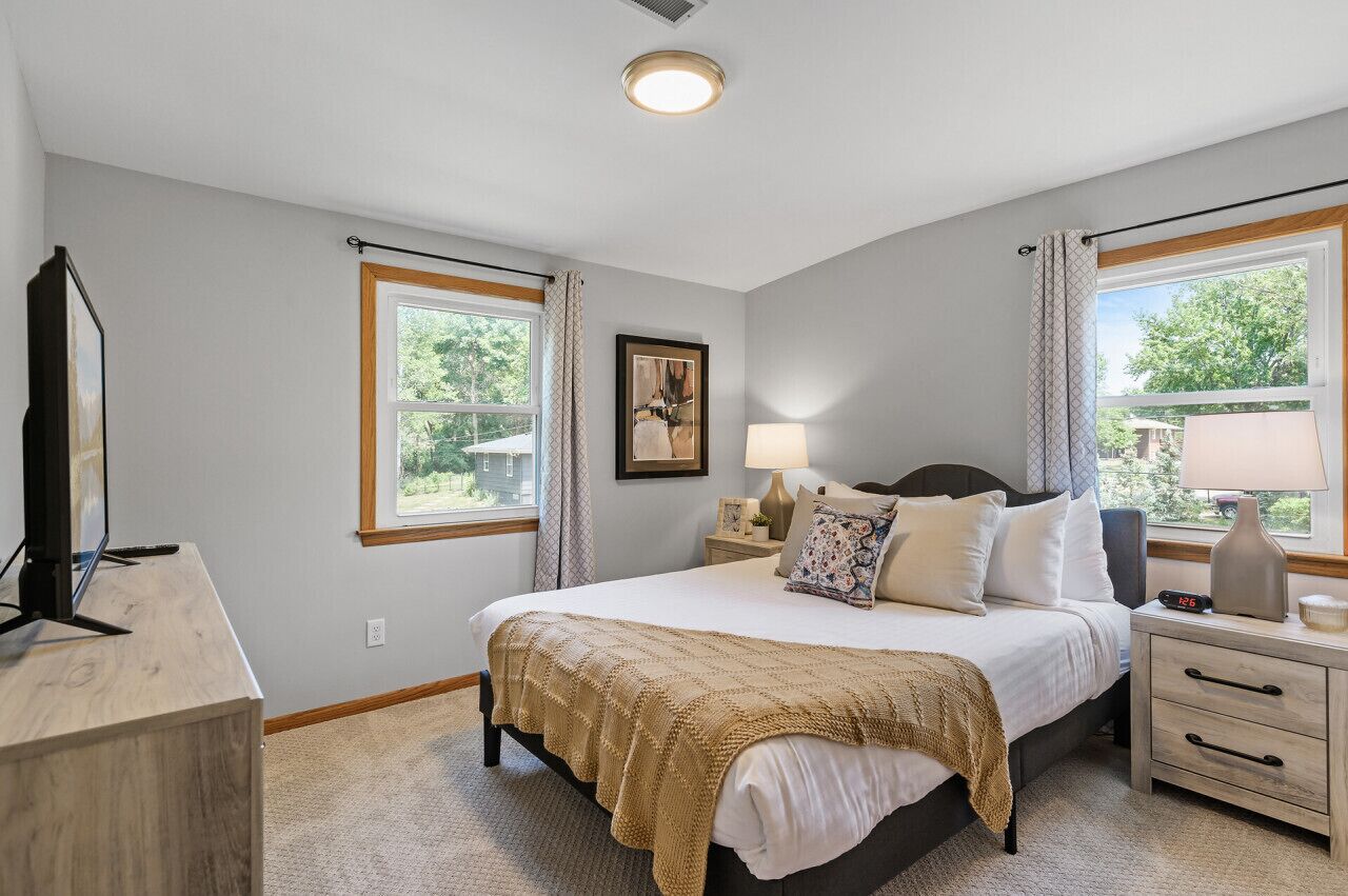 A bedroom with a bed, bedside tables, a lamp, a clock, and a window with curtains.