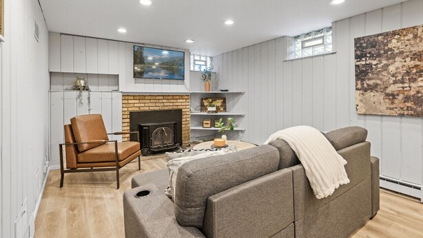 A modern living room with a fireplace, a sofa, a leather armchair, and a painting on the wall.