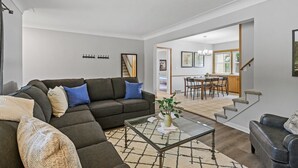 A modern living room with a sectional sofa, a glass coffee table, and a staircase leading to a dining area.