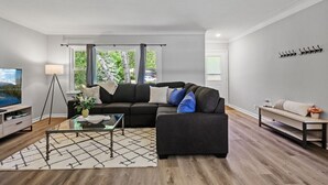 A modern living room with a sectional sofa, a glass coffee table, a floor lamp, and a view of the outdoors through large windows.