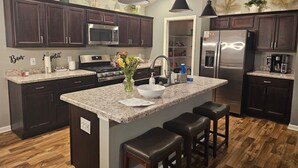 A modern kitchen with dark wood cabinets, stainless steel appliances, a granite countertop, and a central island with bar stools. - St. John's, 3 bdrm, 2 bath, 2022 built home. 10% off military, breast cancer (The Villages)