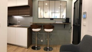 A compact kitchen with white cabinets, a wooden countertop, and two bar stools. - Studio Moderne Proche Champs Elysée (Paris)