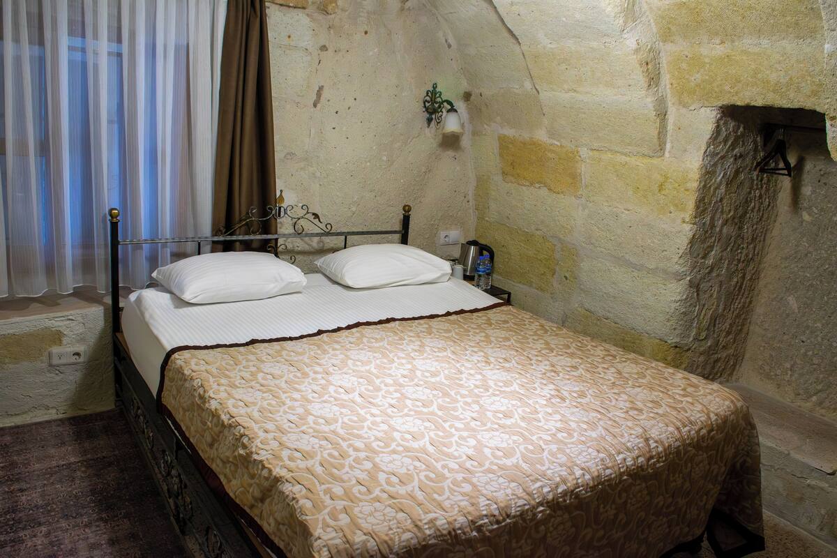 A bed with a patterned bedspread in a room with stone walls and a small wall-mounted light fixture.