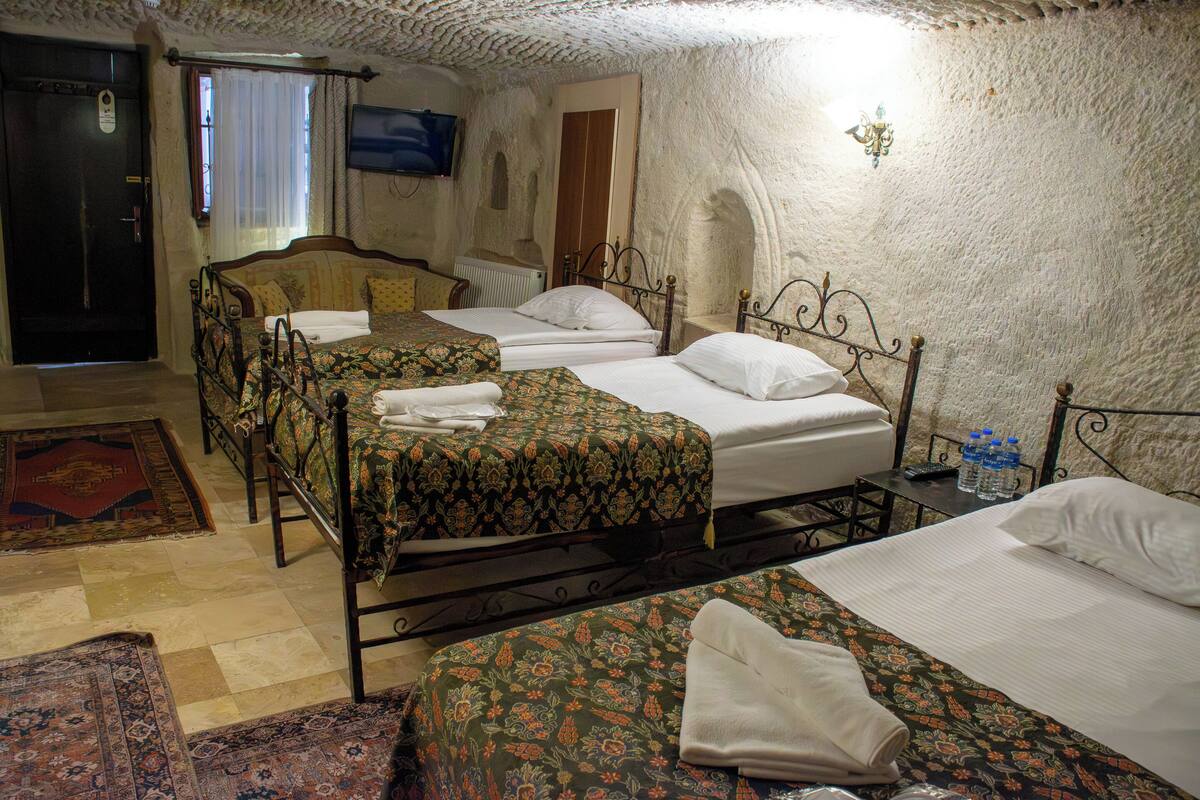 A hotel room with three beds, a television, a radiator, and a patterned rug.