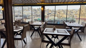 A restaurant with tables and chairs arranged for dining, large windows offering a view of a cityscape. - ALACA CAVE CAPPADOCIA (Nevsehir)