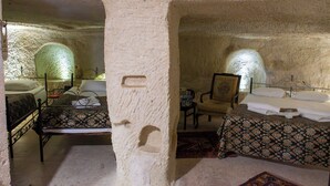 A room with a rustic stone wall, a bed with a patterned bedspread, a chair, and a small table with a lamp. - ALACA CAVE CAPPADOCIA (Nevsehir)