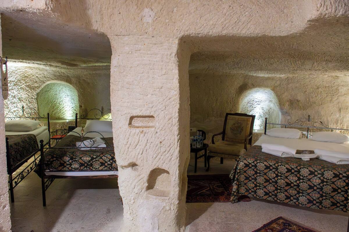 A room with a rustic stone wall, a bed with a patterned bedspread, a chair, and a small table with a lamp.