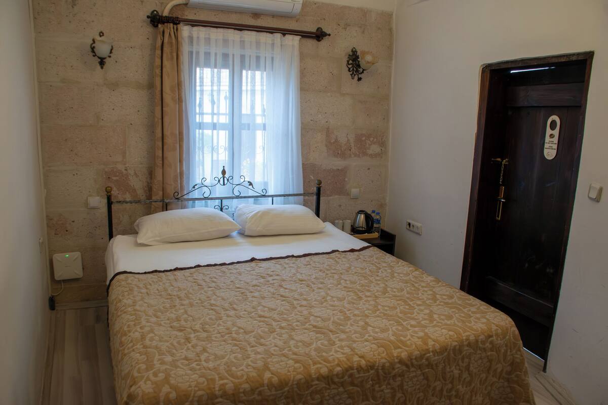 A neatly made bed with a patterned bedspread, a window with sheer curtains, and a door with a lock.