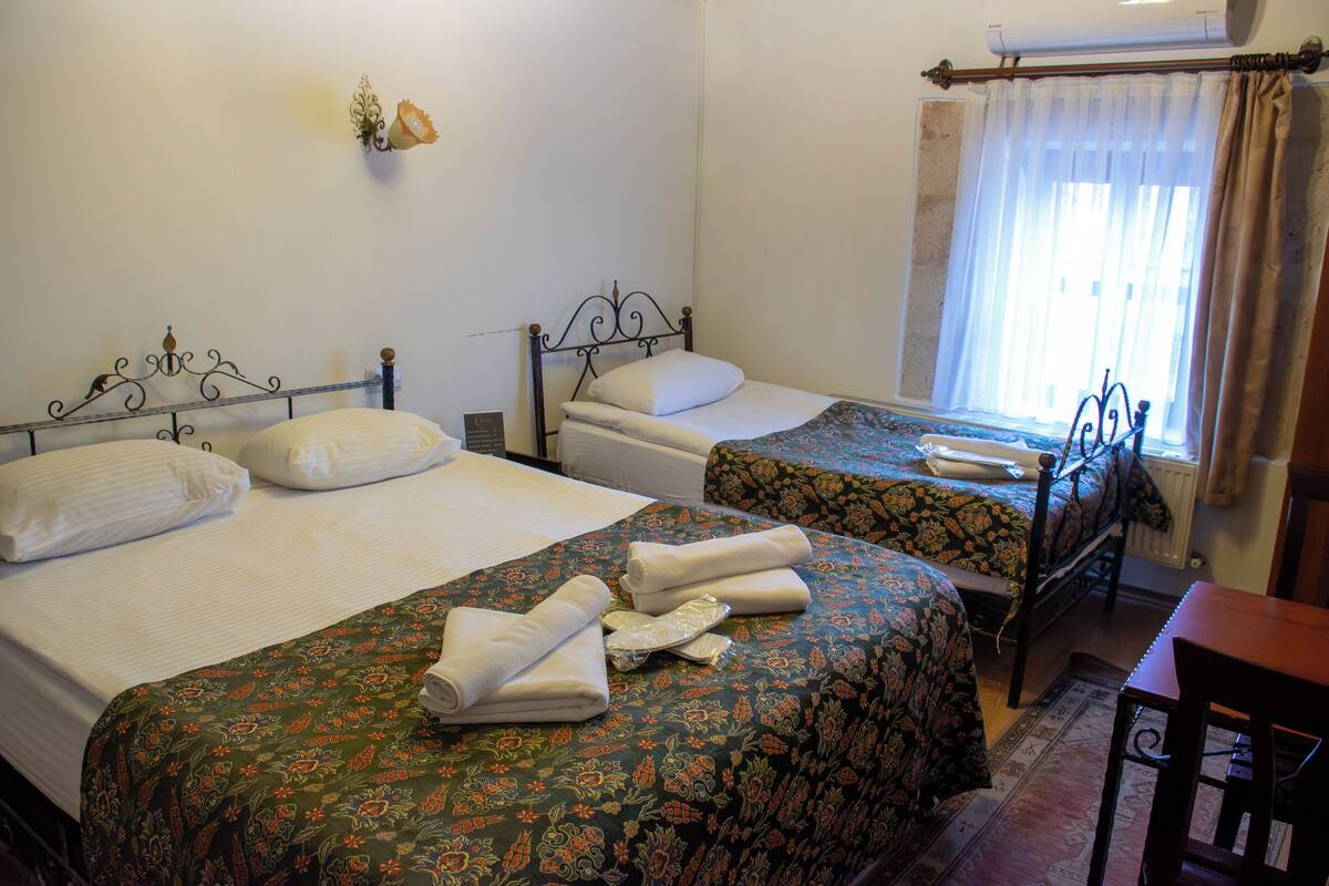 A hotel room with two beds, each with a floral bedspread and white linens. There is a wooden chair and a small table in the corner.