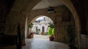 An arched courtyard with stone walls, potted plants, and a view of a building in the background. - ALACA CAVE CAPPADOCIA (Nevsehir)