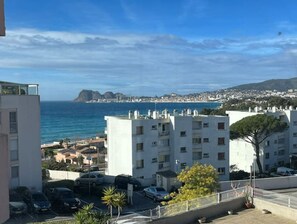 Un quartier résidentiel situé sur la côte, avec des bâtiments blancs, une vue sur la mer et des voitures garées.