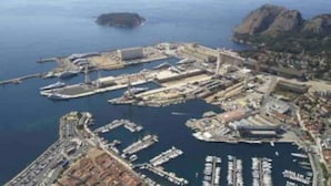 En vy från ovan över en småbåtshamn vid kusten, med flera bryggor och båtar.