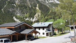 A mountain lodge with a covered parking area, a stone building, and a view of snow-capped mountains. - South-facing studio 4 pers, near center, terrace (Pralognan-la-Vanoise)