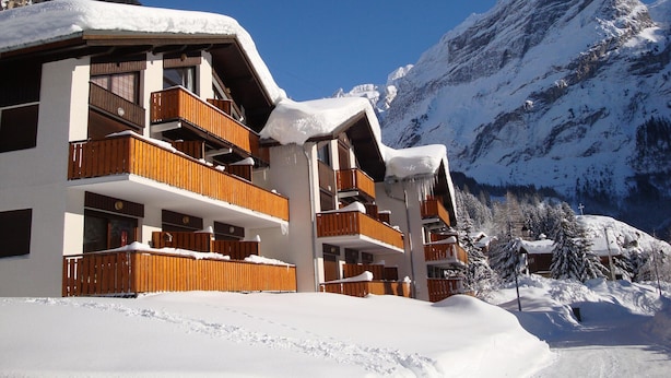 A multi-story hotel with wooden balconies, surrounded by snow-covered mountains and clear skies. - South-facing studio 4 pers, near center, terrace (Pralognan-la-Vanoise)