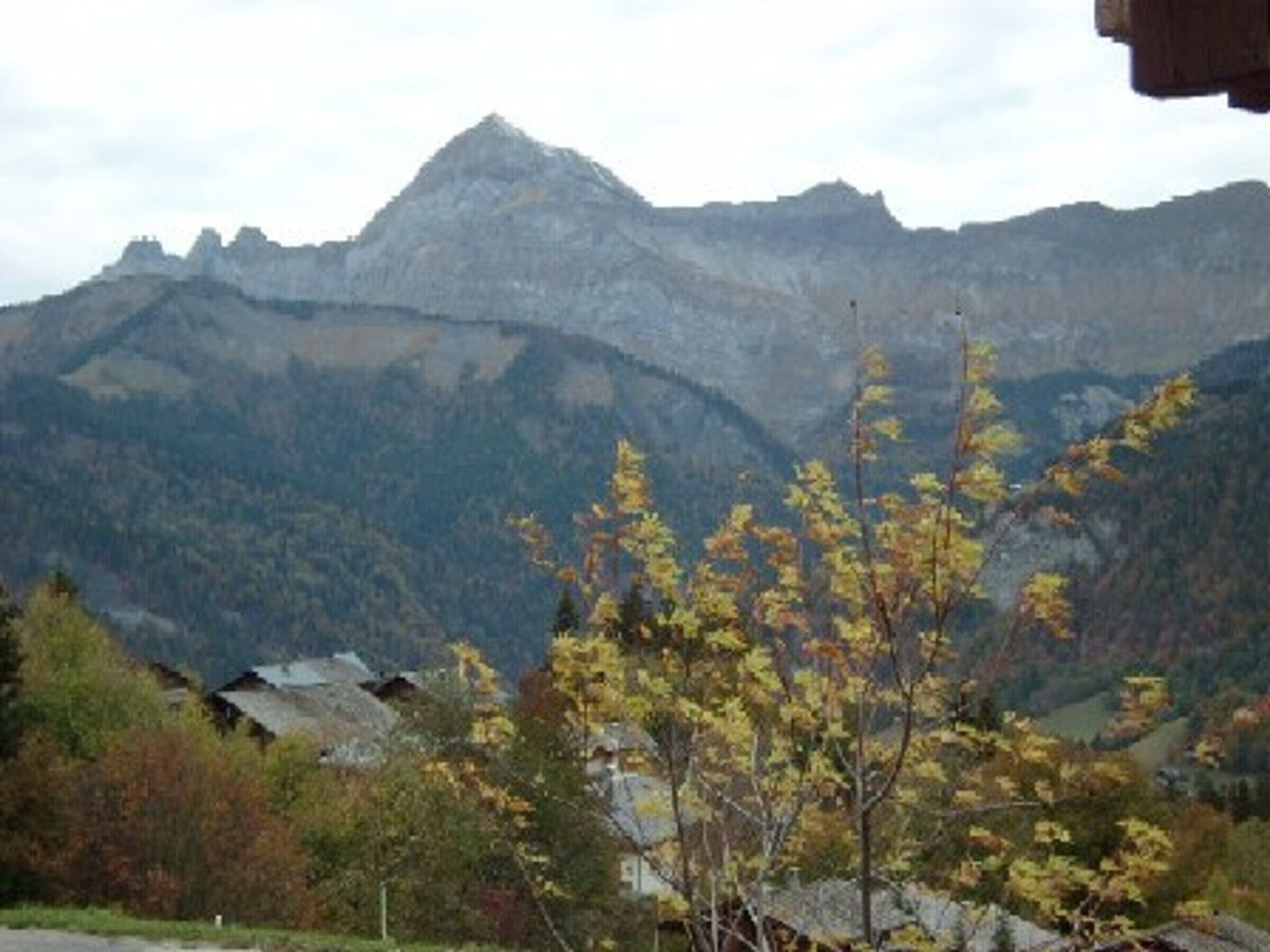 A mountainous landscape with autumn foliage and a few buildings in the foreground.