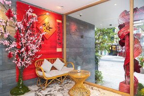 Una habitación con una pared roja, un sofá de mimbre, una mesita redonda y un florero con flores rosas.