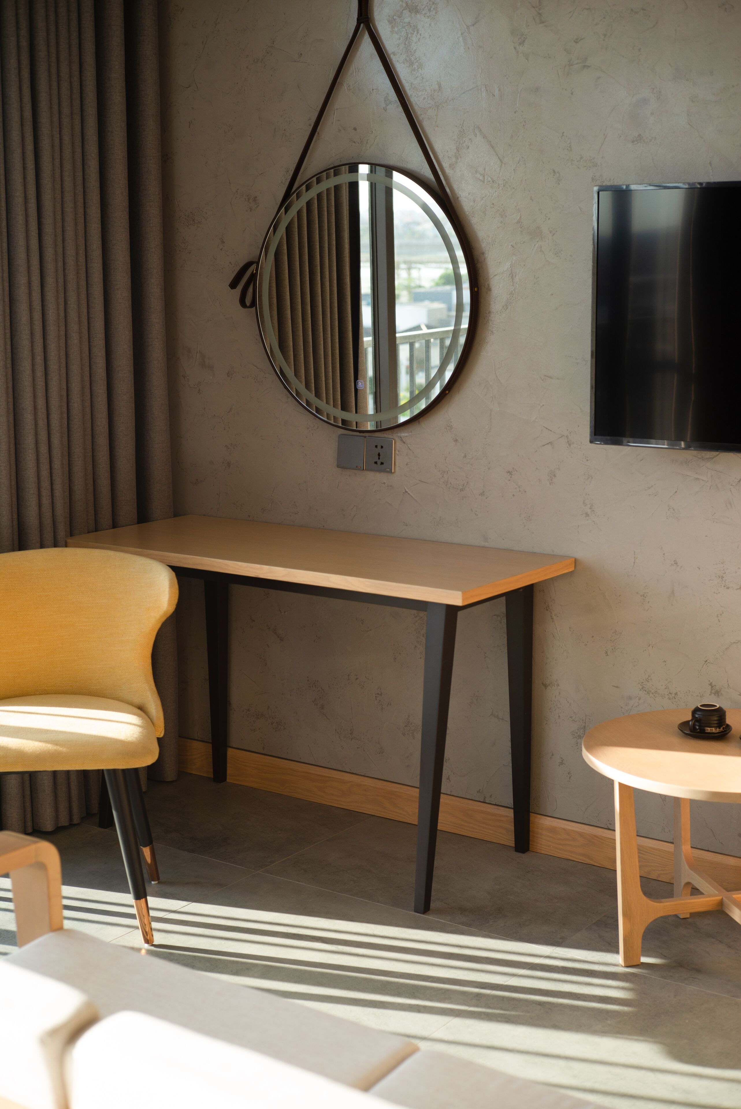 A modern room with a wooden table, a round mirror, a small round table, and a TV mounted on the wall.