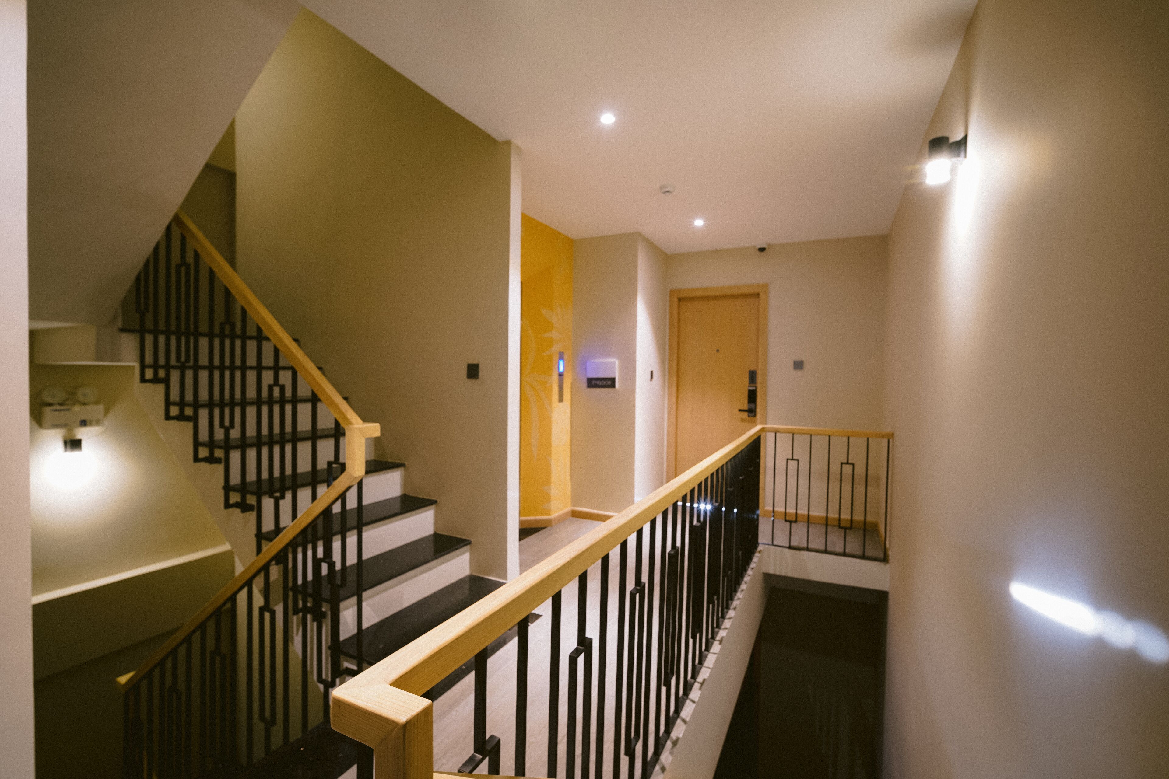 Un escalier moderne avec des rampes noires et des mains courantes en bois, menant à une porte située en haut.