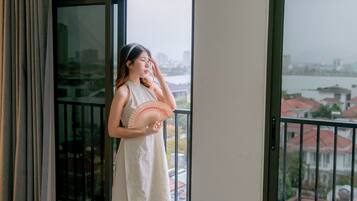 A person standing by a window with a view of a cityscape and a body of water.