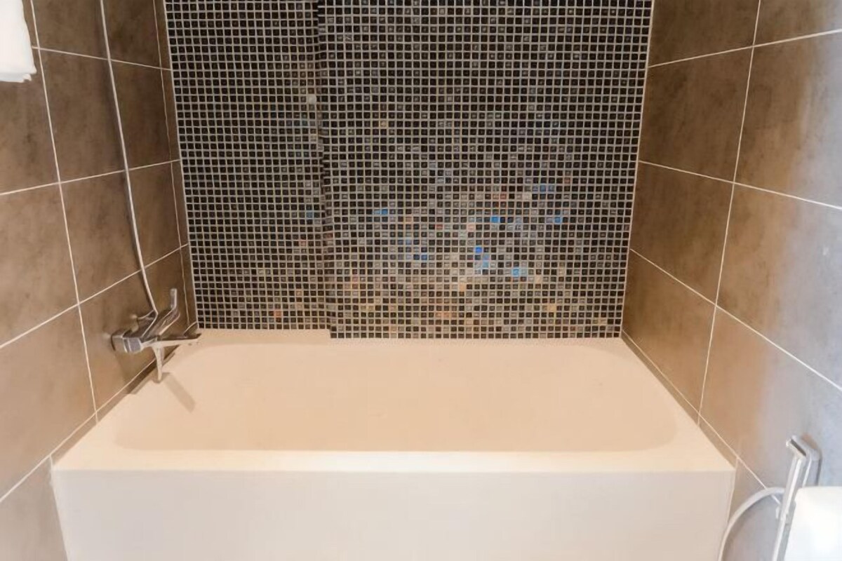A bathtub with a mosaic wall, tiled floor, and a shower area.