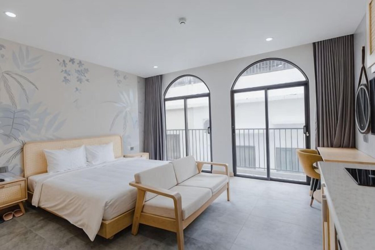 A bedroom with a bed, a sofa, a desk, and a balcony with curtains.