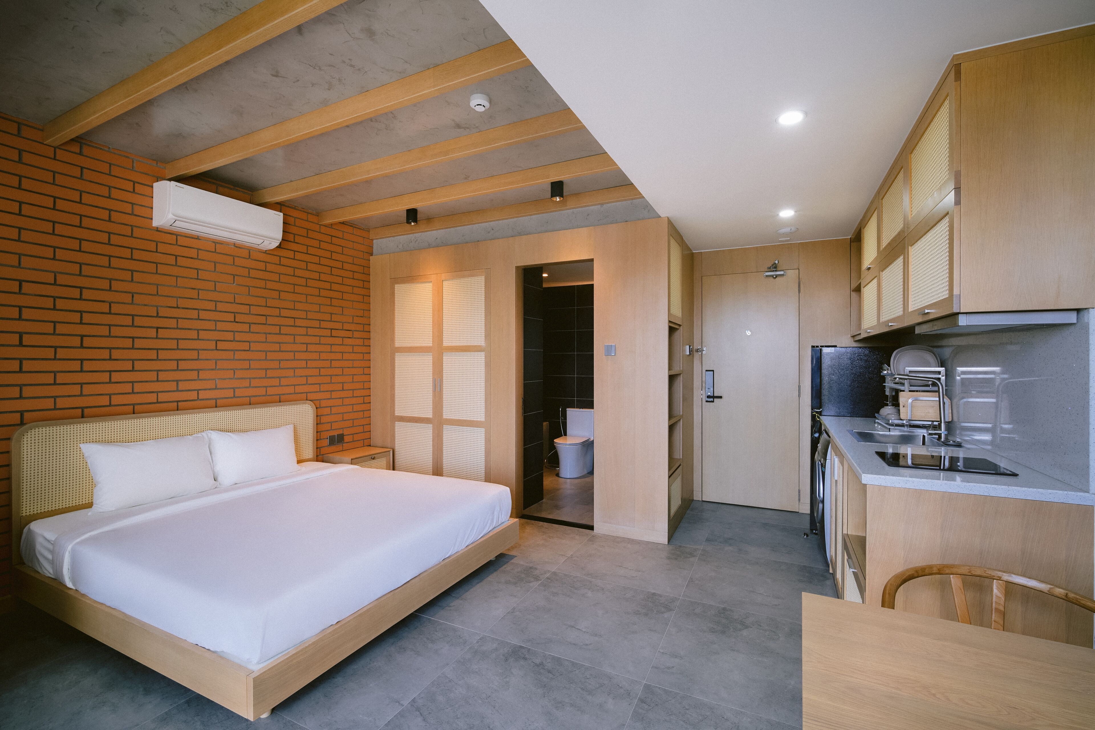 A modern hotel room with a large bed, a kitchenette, and a bathroom visible through an open door.