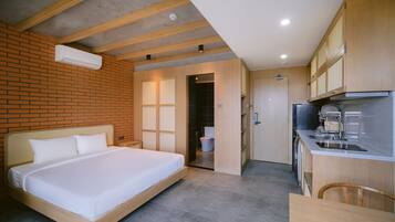 A modern hotel room with a large bed, a kitchenette, and a bathroom visible through an open door.