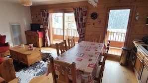 A wooden cabin with a dining table, chairs, a TV, and a fireplace.