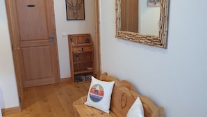 A wooden sofa with a decorative pillow, a small wooden shelf with books, and a mirror on the wall.