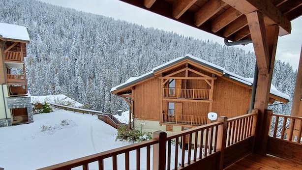 A wooden cabin with a balcony, surrounded by snow-covered trees.