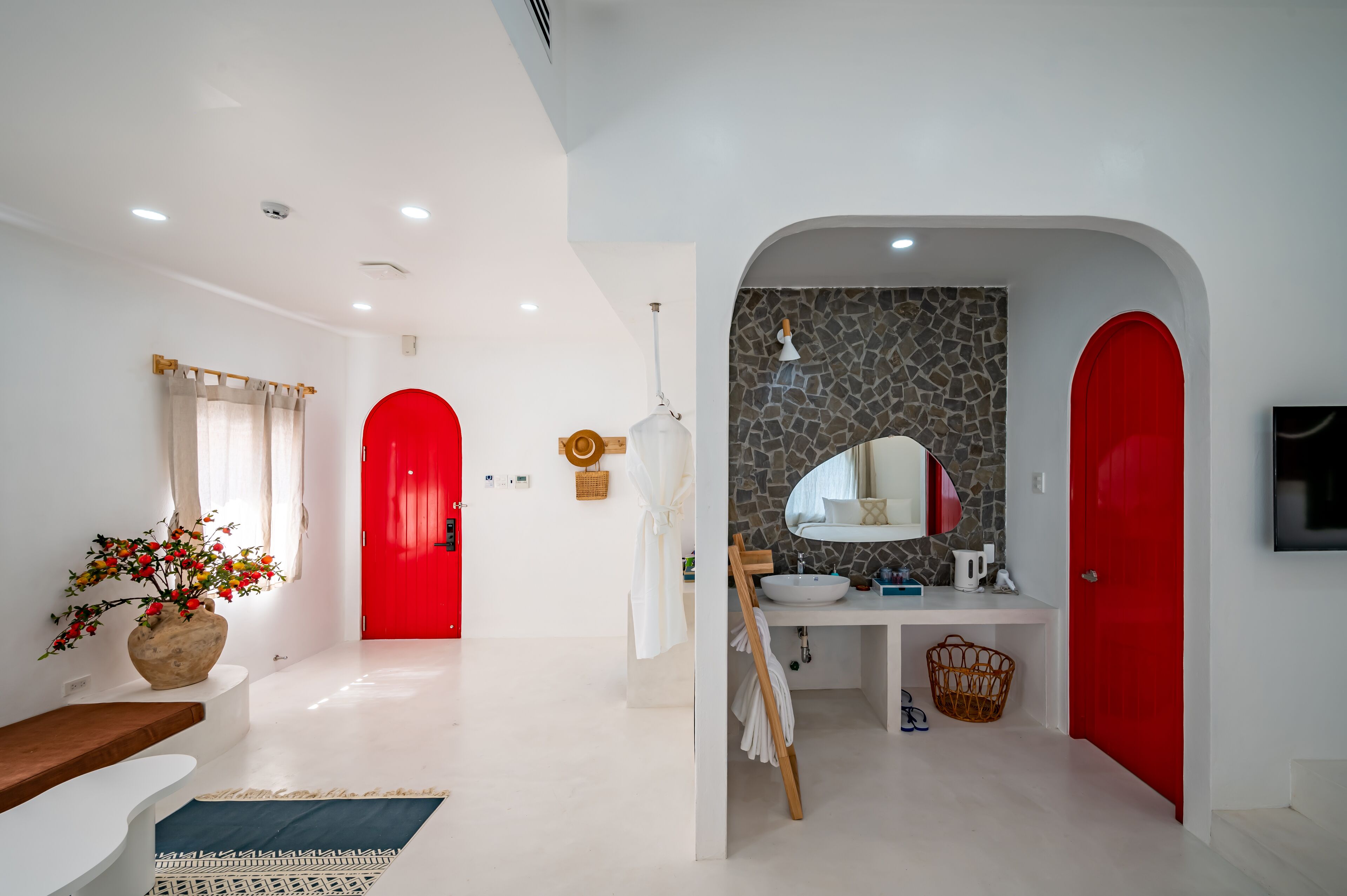 A modern bathroom with a stone backsplash, a white sink, and a red door.
