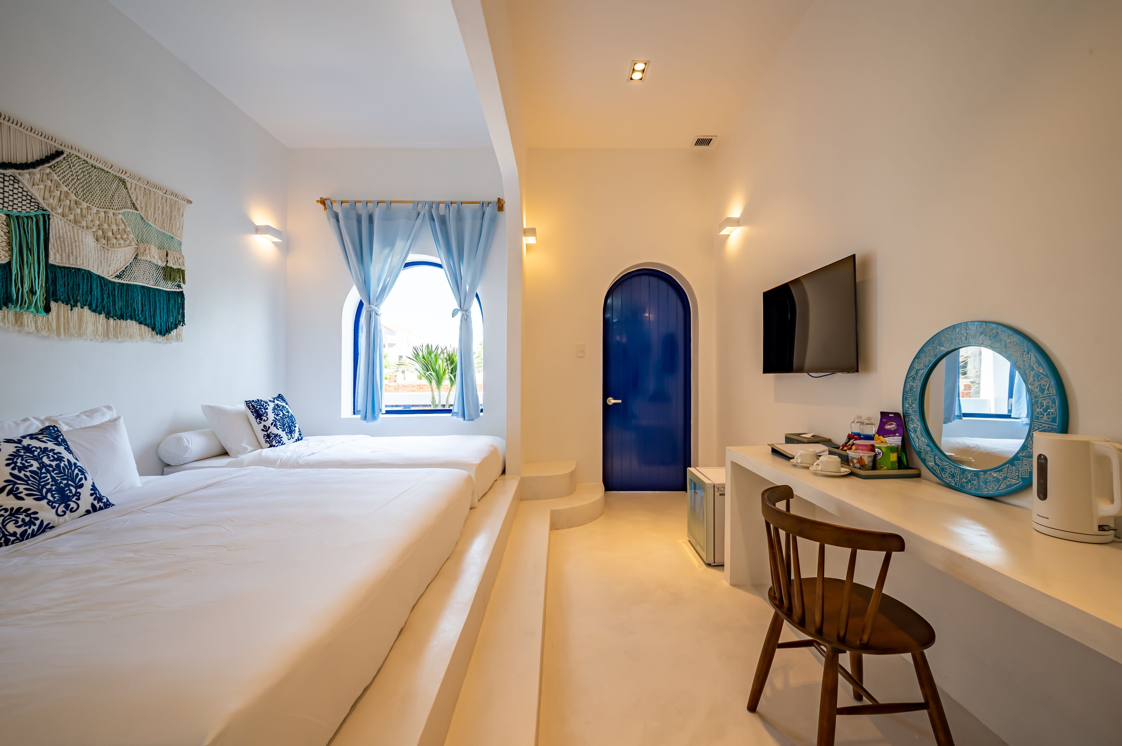 A hotel room with two beds, a desk with a chair, a TV, a coffee maker, and a large mirror.