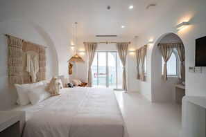 Une chambre spacieuse avec un grand lit, une décoration murale en macramé et une vue sur la ville depuis les portes du balcon.