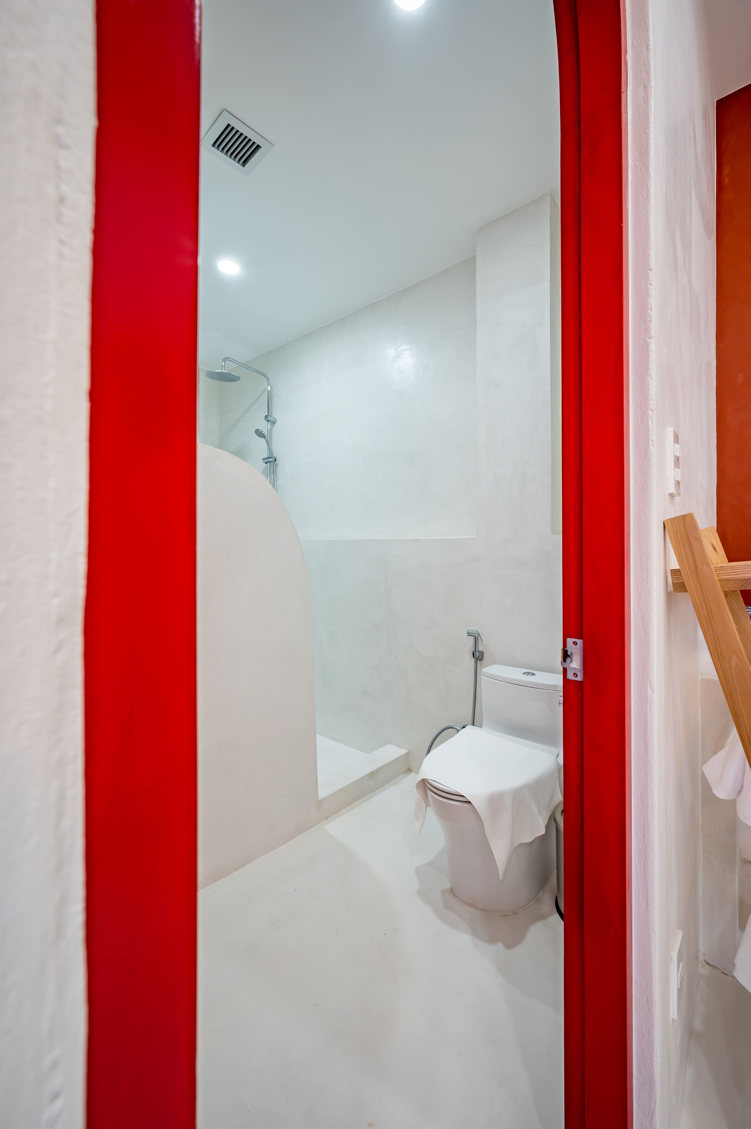 Een badkamer met een douche, toilet en een rode deurkozijn.