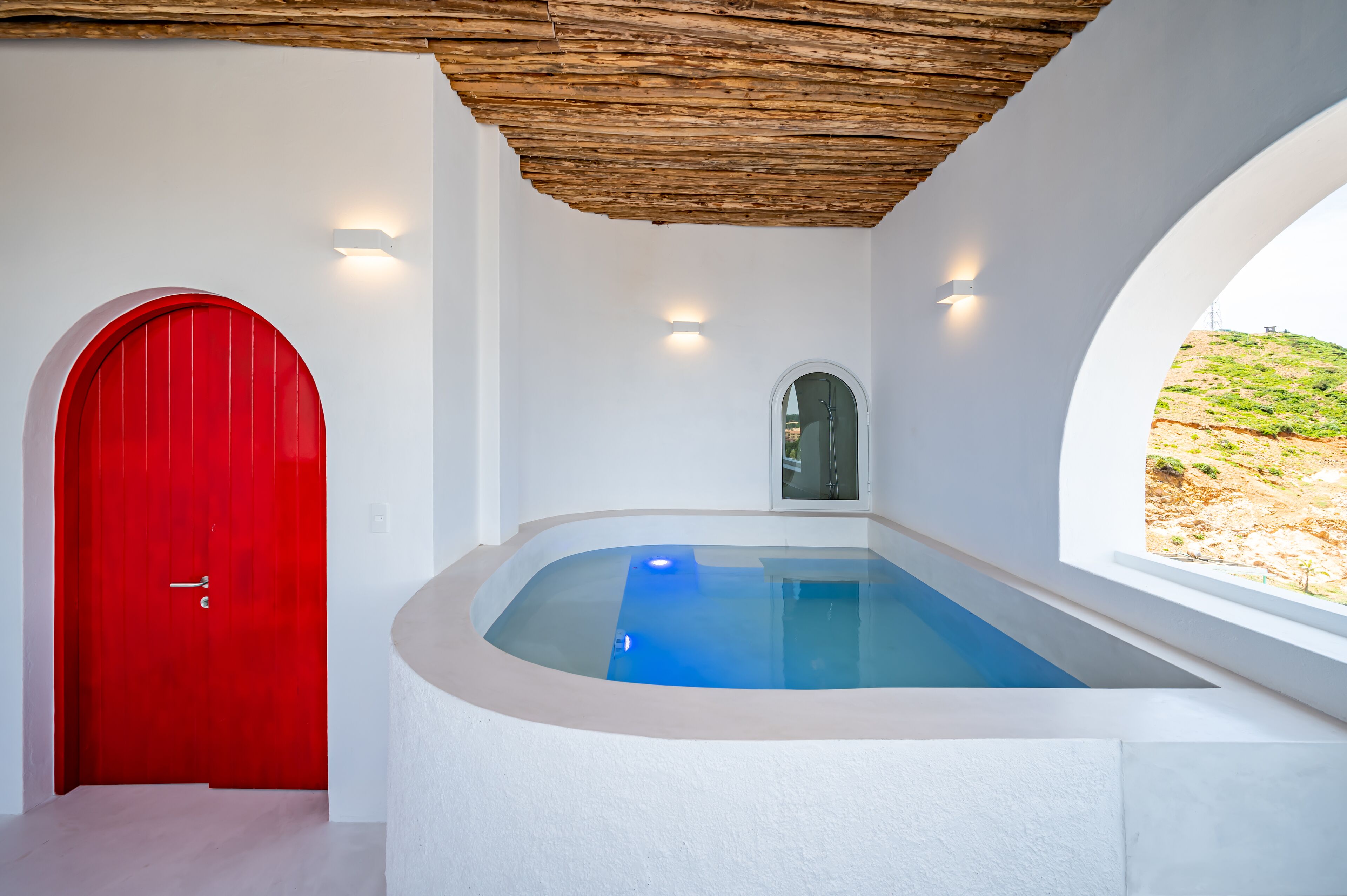 A modern bathroom with a red door, a small window, and a built-in bathtub.